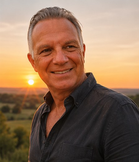 Siegfried lächelt in die Kamera, im Hintergrund ein Sonnenuntergang über weiter Landschaft.